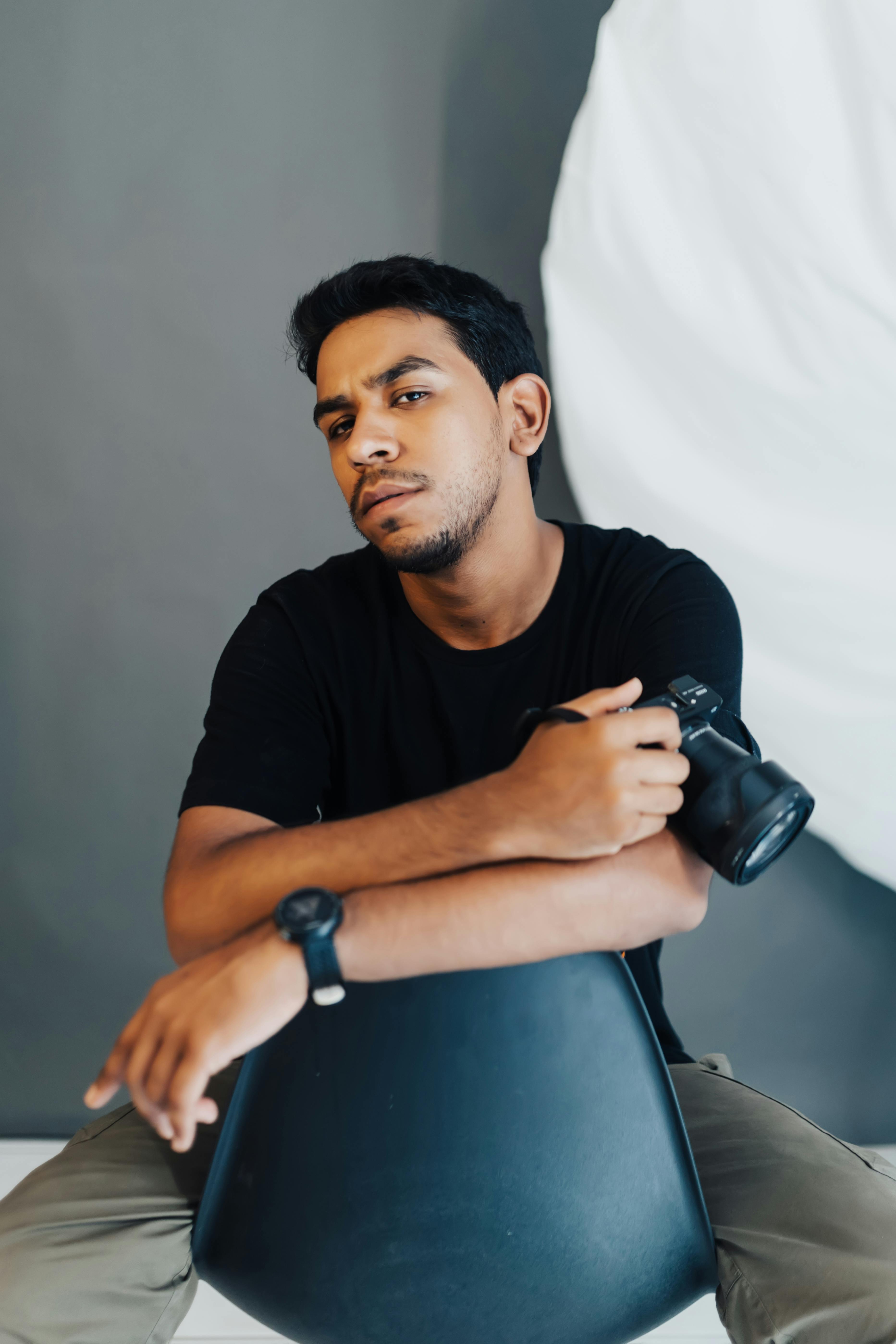 Man with camera sitting on chair in studio. Calm and professional ambiance.