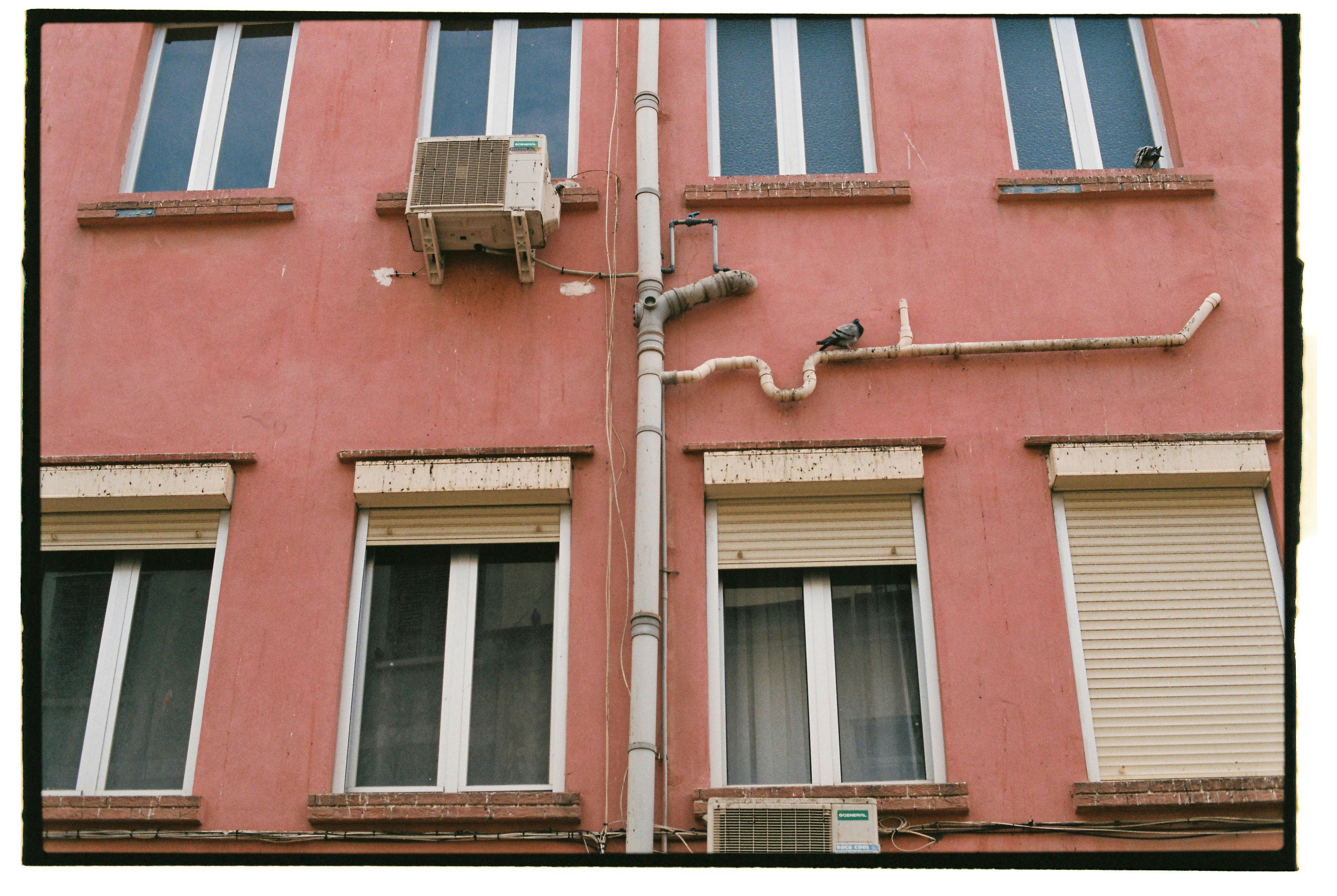 Close-up of a red residential building facade featuring windows and exposed pipes in Gibraltar.