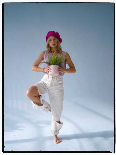 Stylish woman in pink beret holding a fern indoors with a baby blue backdrop.