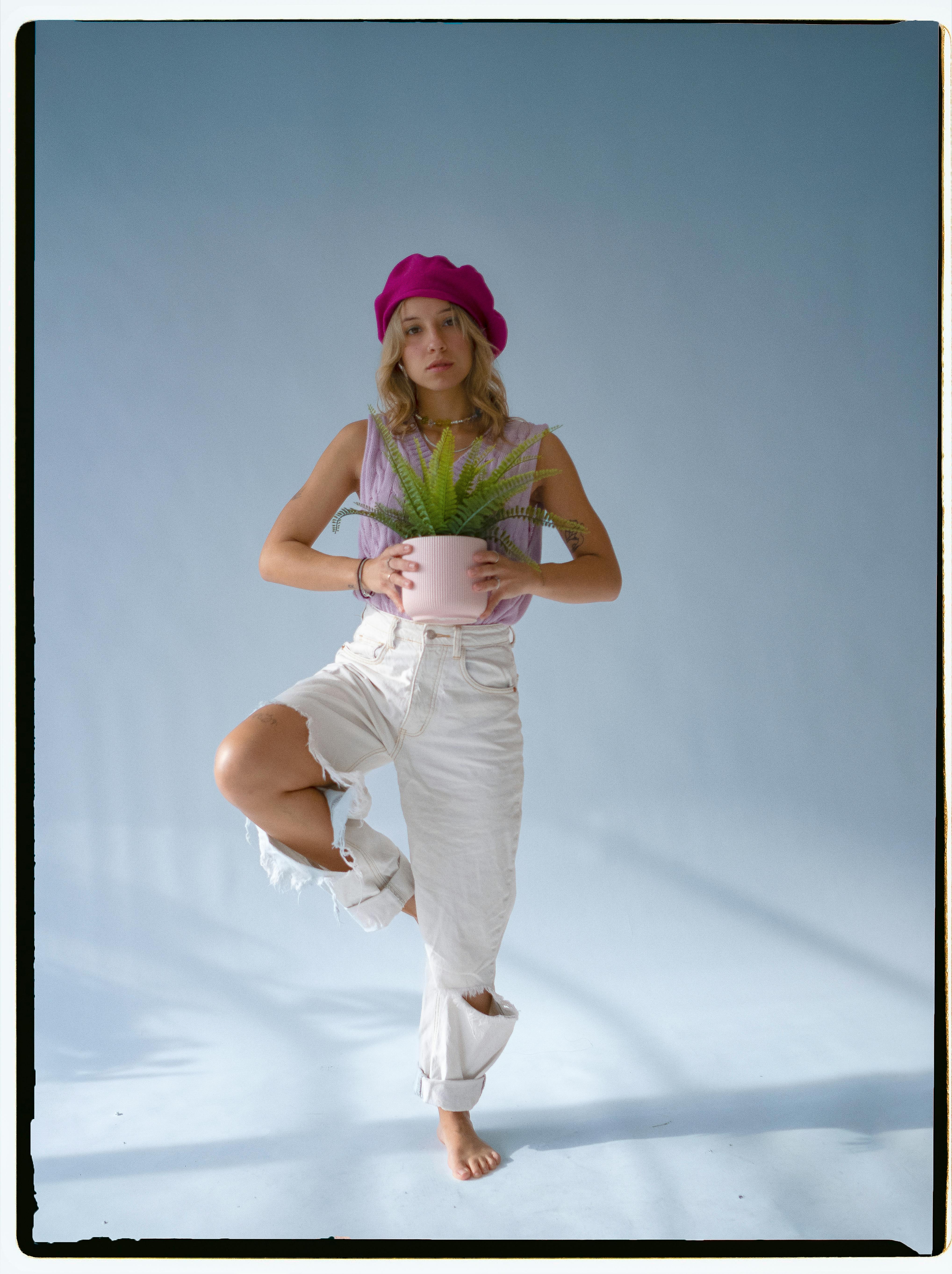 Free Stylish woman in pink beret holding a fern indoors with a baby blue backdrop. Stock Photo