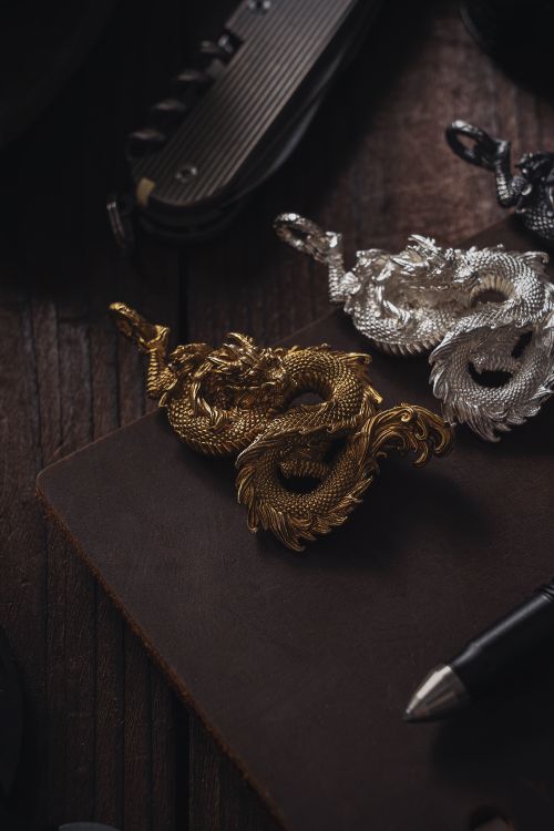 Free Golden and silver dragon pendants on a rustic desk with a pen, perfect for design inspiration. Stock Photo