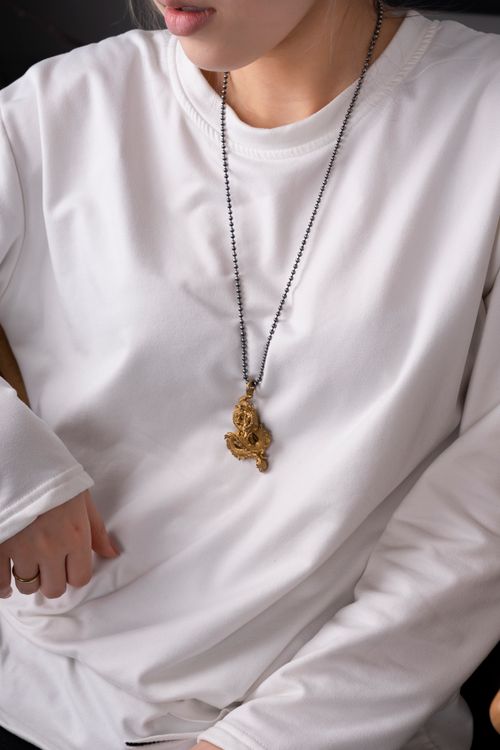Free Close-up of a gold pendant necklace with a dragon design worn over a white shirt. Stock Photo