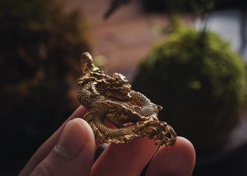 Free Close-up of a detailed golden dragon pendant held between fingers, highlighting craftsmanship. Stock Photo