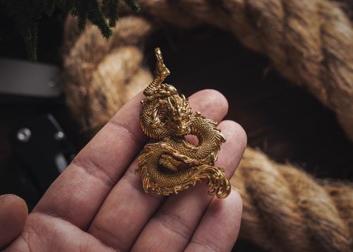 Free Close-up of a hand holding an ornate golden dragon pendant against a textured background. Stock Photo
