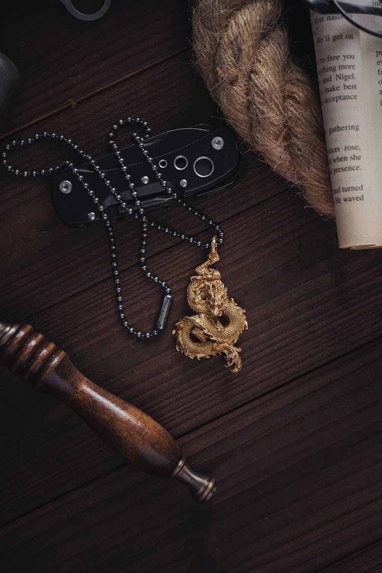 A Golden Dragon Pendant With A Silver Chain Lying On A Desk 