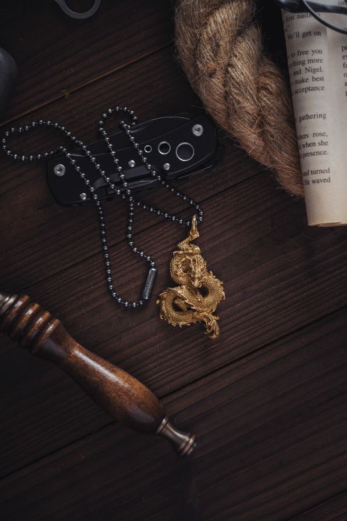 Free Close-up of a detailed dragon pendant on a dark wooden surface with decorative items. Stock Photo