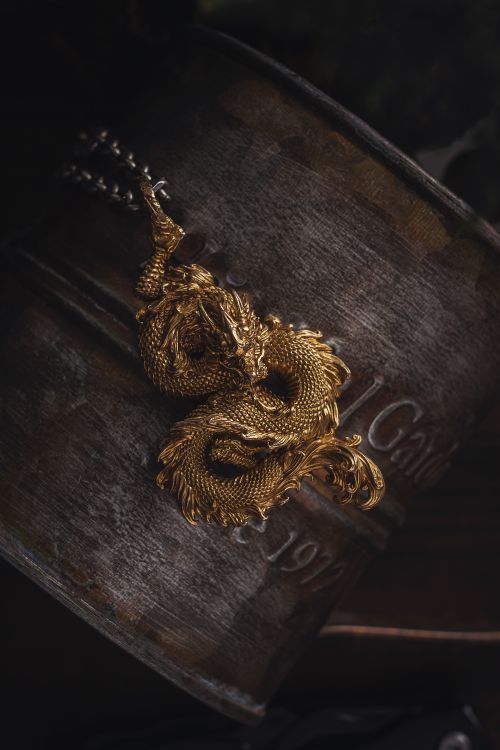 Free Elegant golden dragon pendant displayed against a textured, rustic background. Perfect for jewelry lovers. Stock Photo