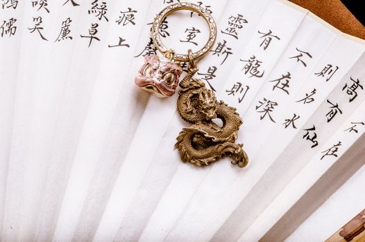 Close-up of a golden dragon pendant on a decorative fan with Asian script.
