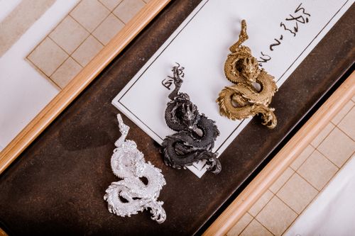 Free Three intricately crafted dragon pendants in gold, silver, and bronze on a decorative surface. Stock Photo
