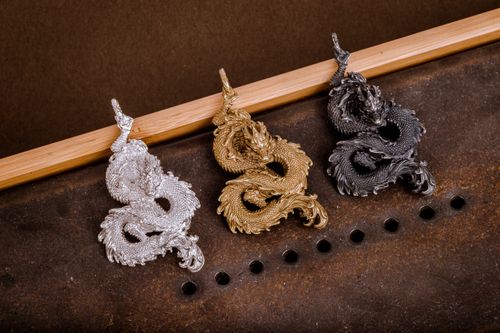 Free A stunning display of silver, gold, and black dragon-shaped metal pendants on a textured surface. Stock Photo