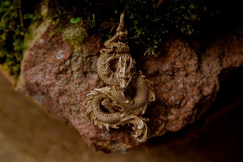 Free Close-up of a beautifully crafted dragon pendant in detailed metalwork, set on a textured rock background. Stock Photo