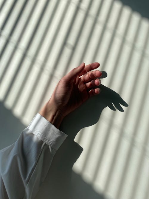 Close-up of an Arm and Hand against a White Wall with Striped Shadows 