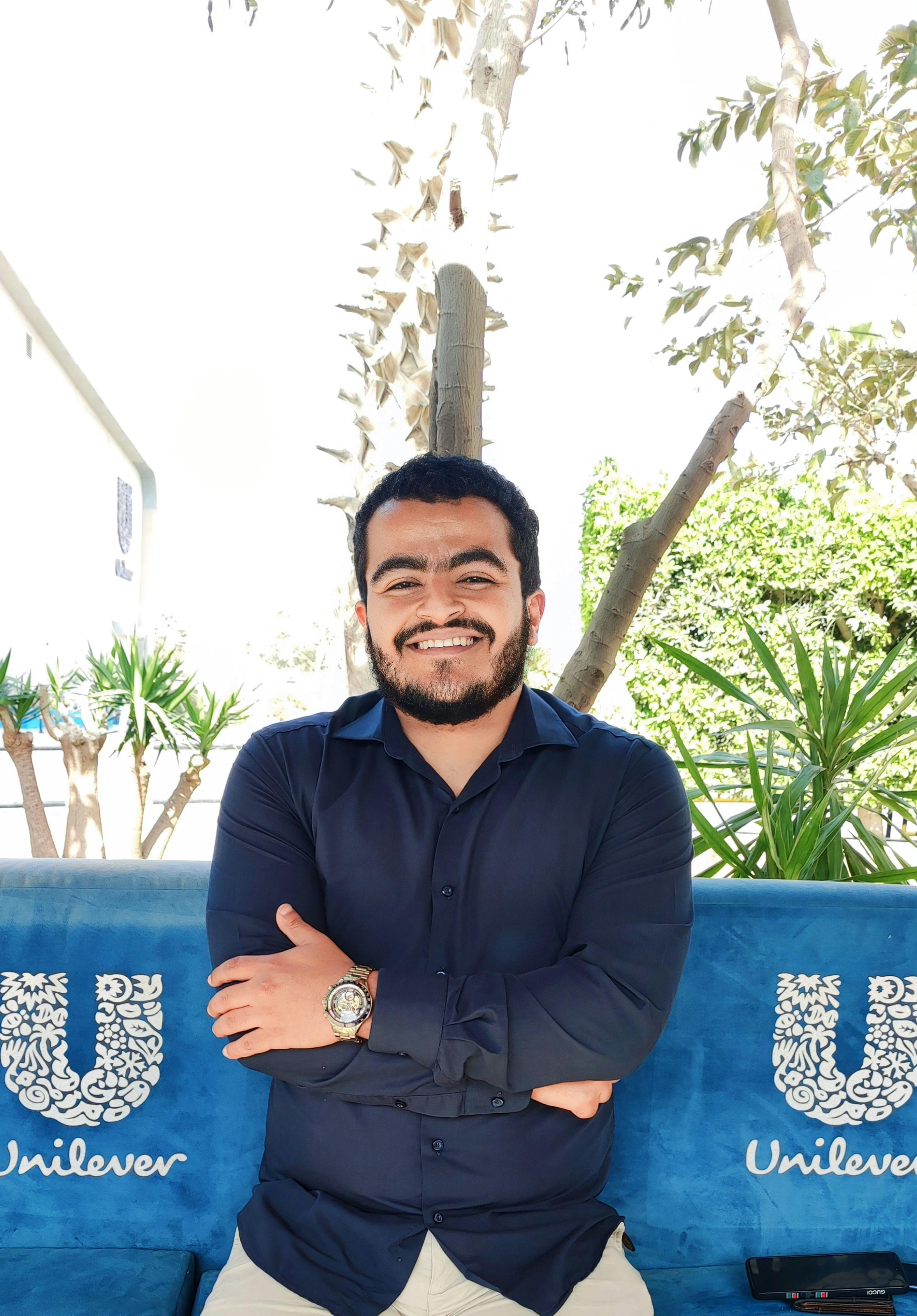 Happy man with arms crossed, wearing a navy blue shirt, smiling outdoors.