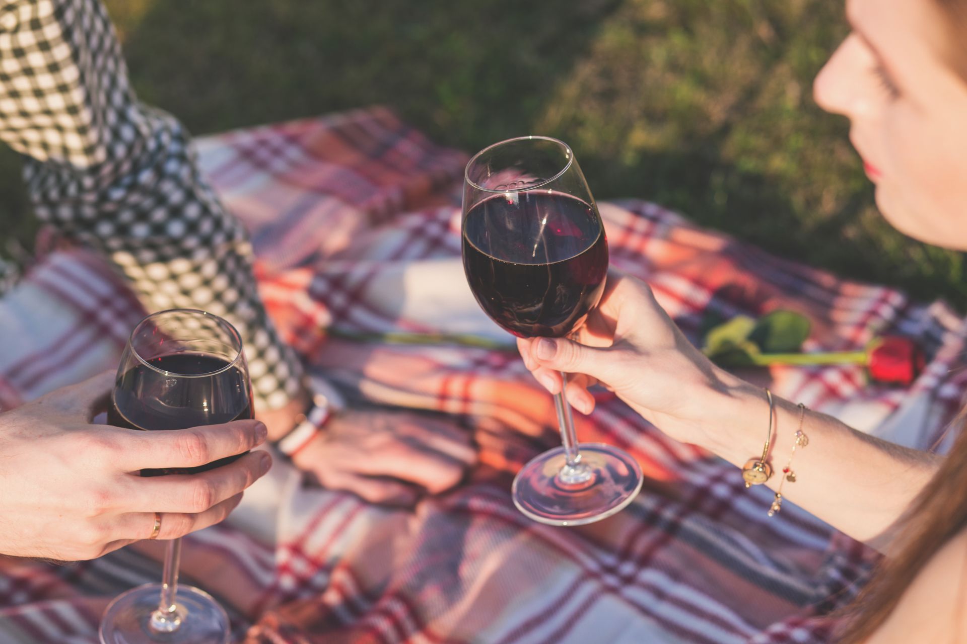 A couple enjoying a romantic picnic with wine and roses on a sunny day outdoors.