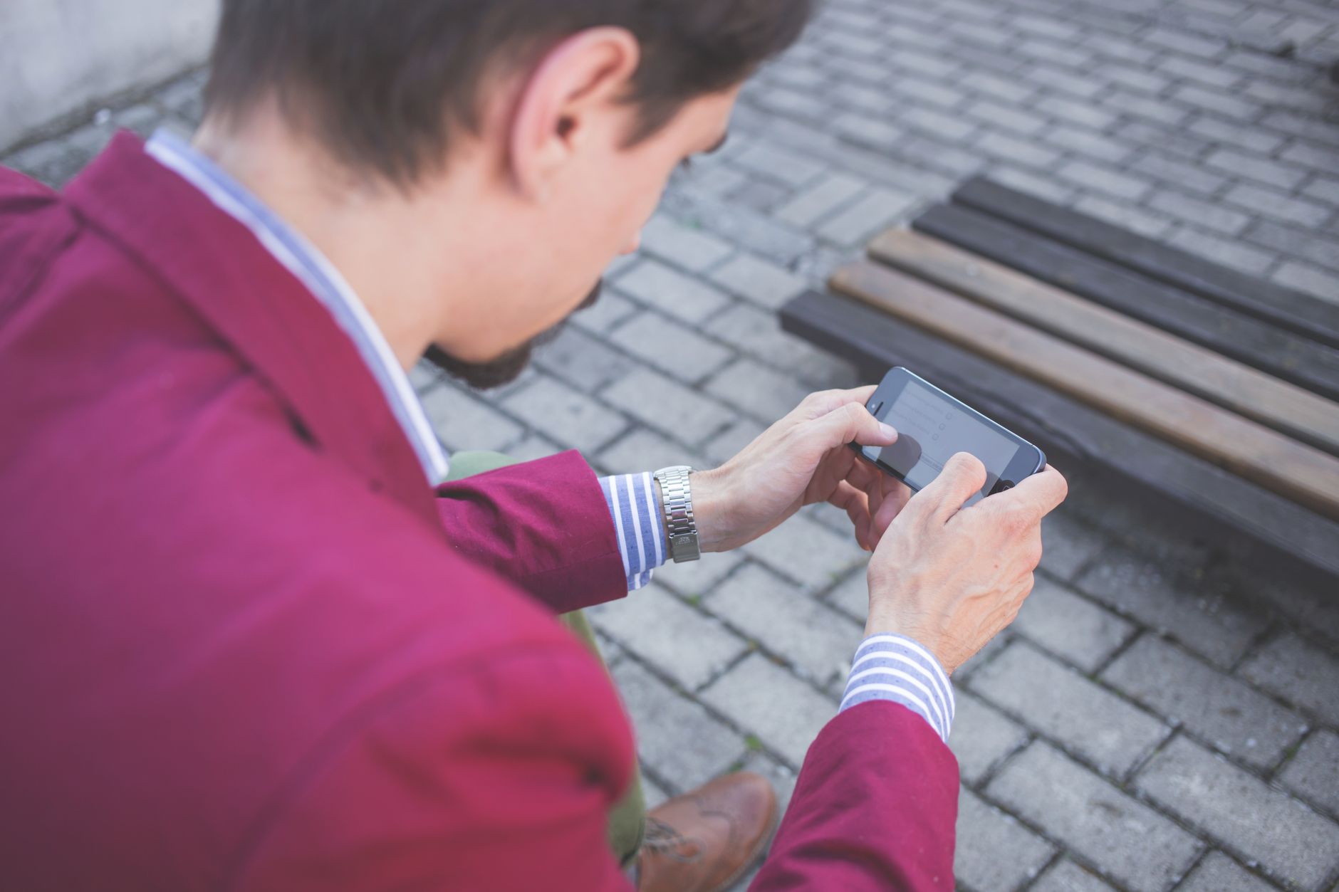 A person using a smartphone on cobblestone pavement outdoors, viewed from behind.