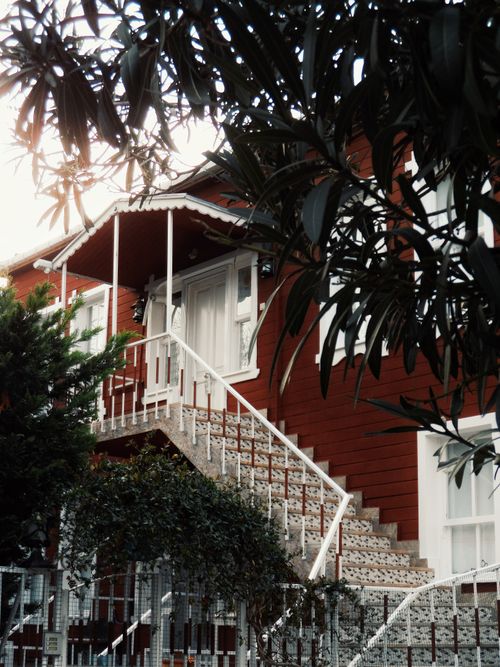 Free Rustic red house exterior featuring a unique staircase surrounded by lush greenery. Stock Photo