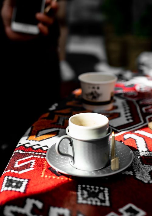 Free A porcelain coffee cup sits on a colorful patterned tablecloth. Ideal for lifestyle settings. Stock Photo