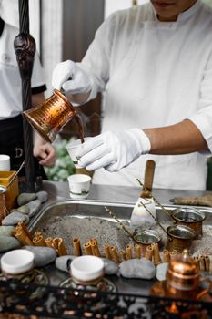 A person expertly pouring Turkish coffee from a cezve in a traditional setup.