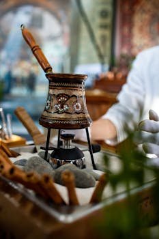 Close-up of a traditional coffee brewing pot on sand with intricate patterns indoors.