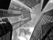 从低角度仰望现代摩天大楼，玻璃幕墙上映照着多云的天空