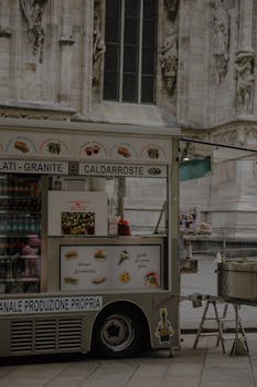 Street food cart offering snacks near Milan's iconic cathedral during daytime.