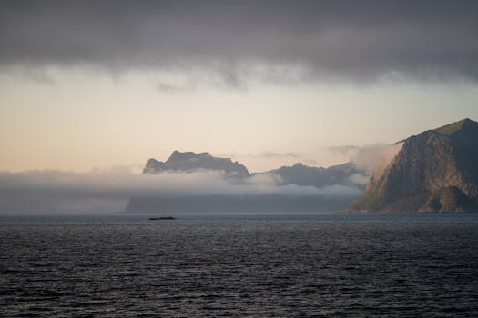 Tranquil view of Reine in Norway with fjords and mist under dramatic sky at sunrise.