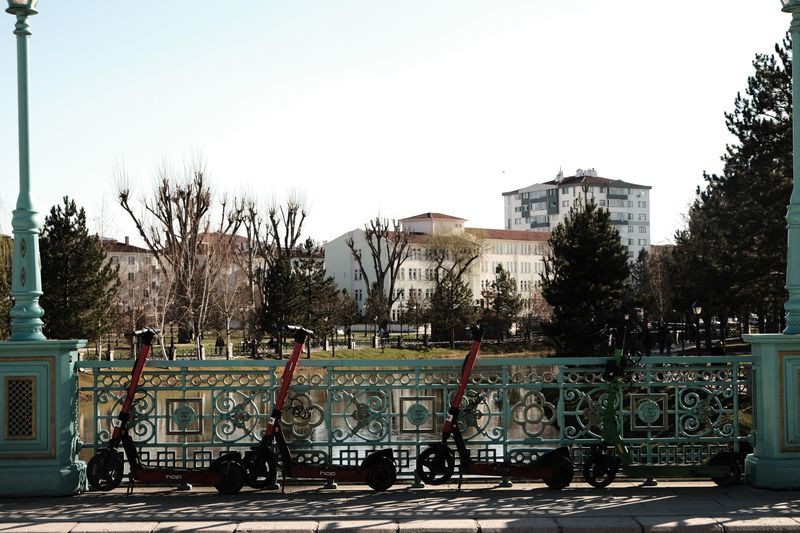 Ornate railing with scooters in a park setting, urban area, bright day.