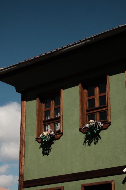 Beautiful green house facade with wooden windows and vibrant flower decorations under a clear blue sky.