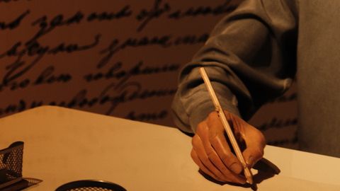 Close-up of hand writing at a desk with vintage decor and warm lighting.