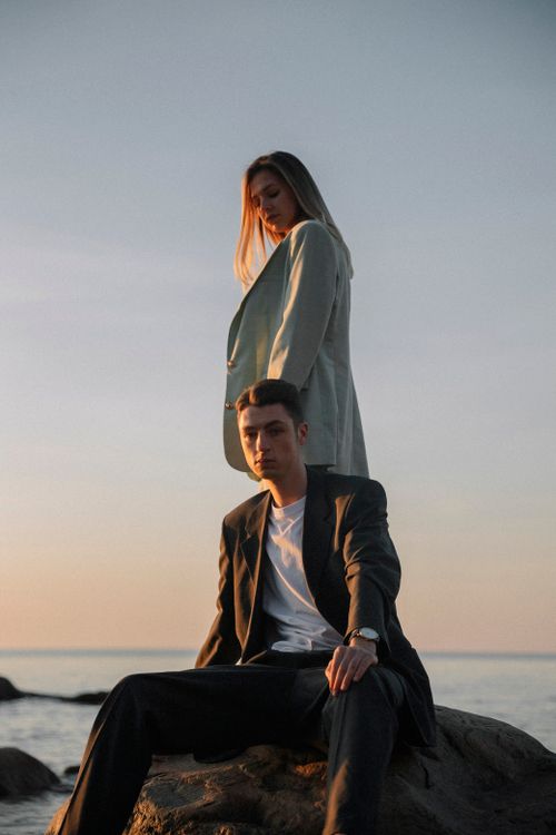 Free Couple posing in stylish outfits on a rocky beach during sunset in Riga, Latvia. Stock Photo