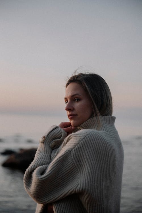 Young Woman in a Sweater Standing on a Beach at Sunset