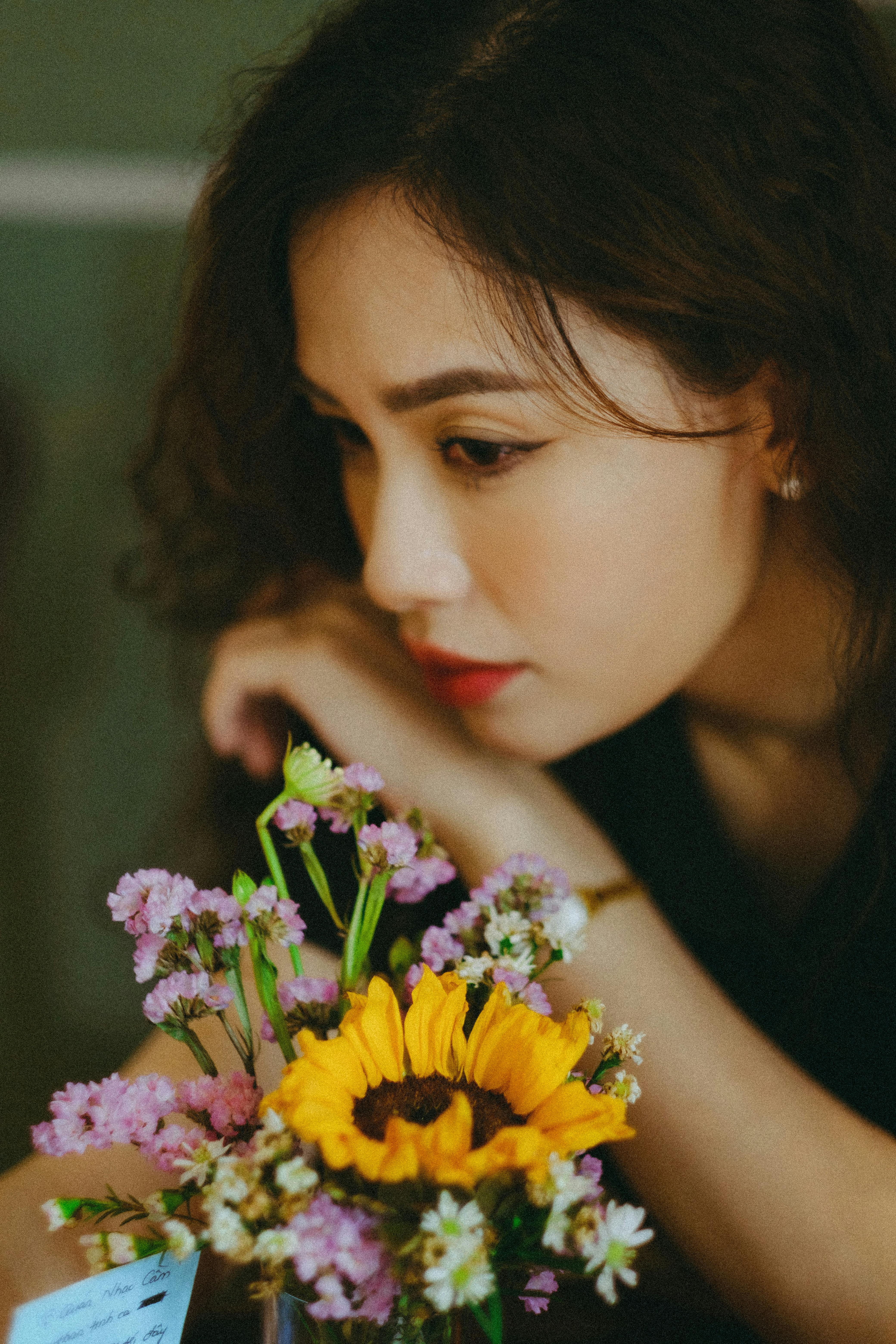 Portrait of a woman gazing thoughtfully at a vibrant floral bouquet indoors.