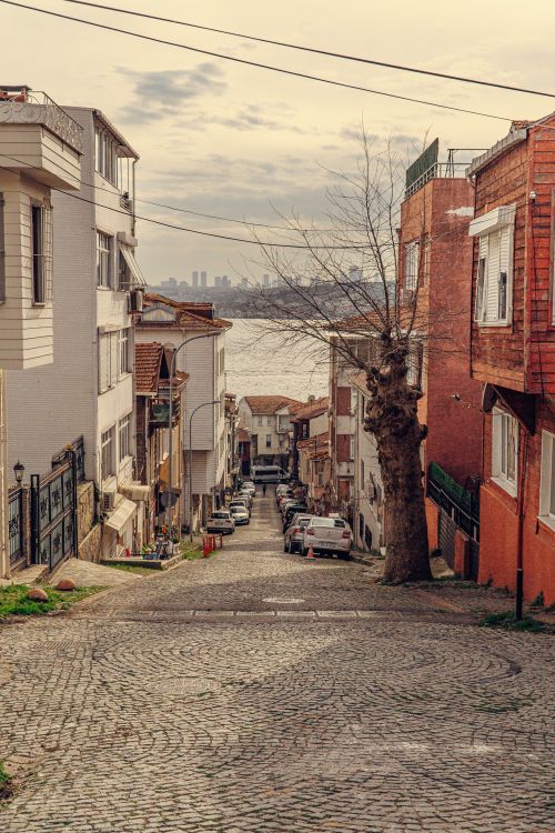 Free Charming city alley leading to a waterfront with distant skyline view. Stock Photo