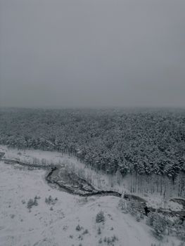 Aerial view of snow-covered forest and river in Mežciems, Latvia, during winter.