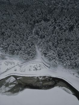 Aerial view of snow-covered forest and winding river in Mežciems, Latvia during winter.