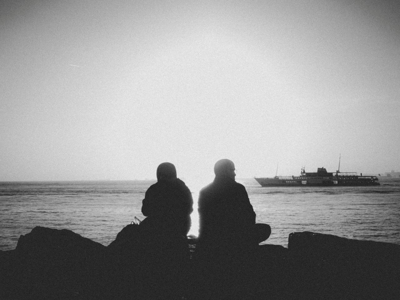 peaceful silhouette of two people sitting by the sea at sunrise with a