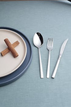 Simple table setting featuring cinnamon sticks, plates, and cutlery on a blue background.