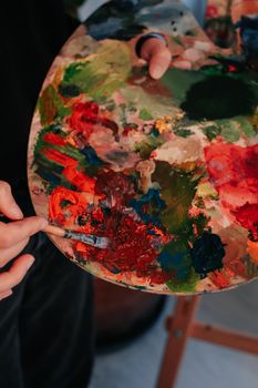 Close-up of a hand holding a vibrant paint palette and brush in use.