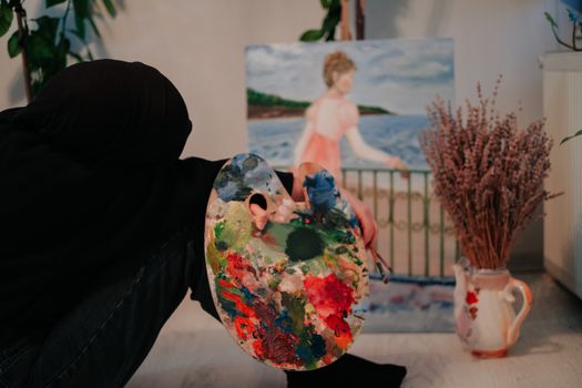 An artist uses a colorful palette while completing an indoor painting.