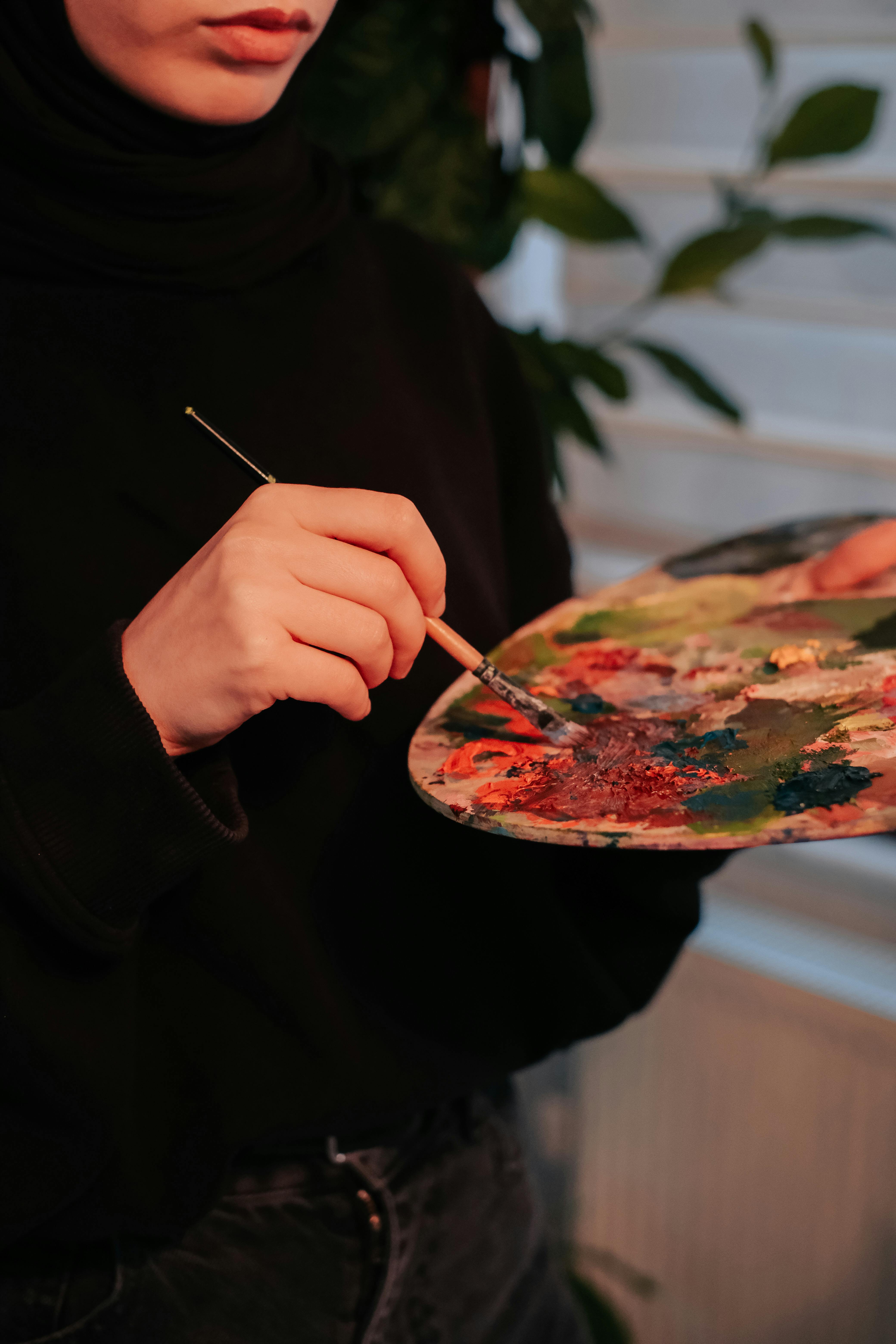 Close-up of an artist mixing colors on a palette with sunlight filtering indoors.