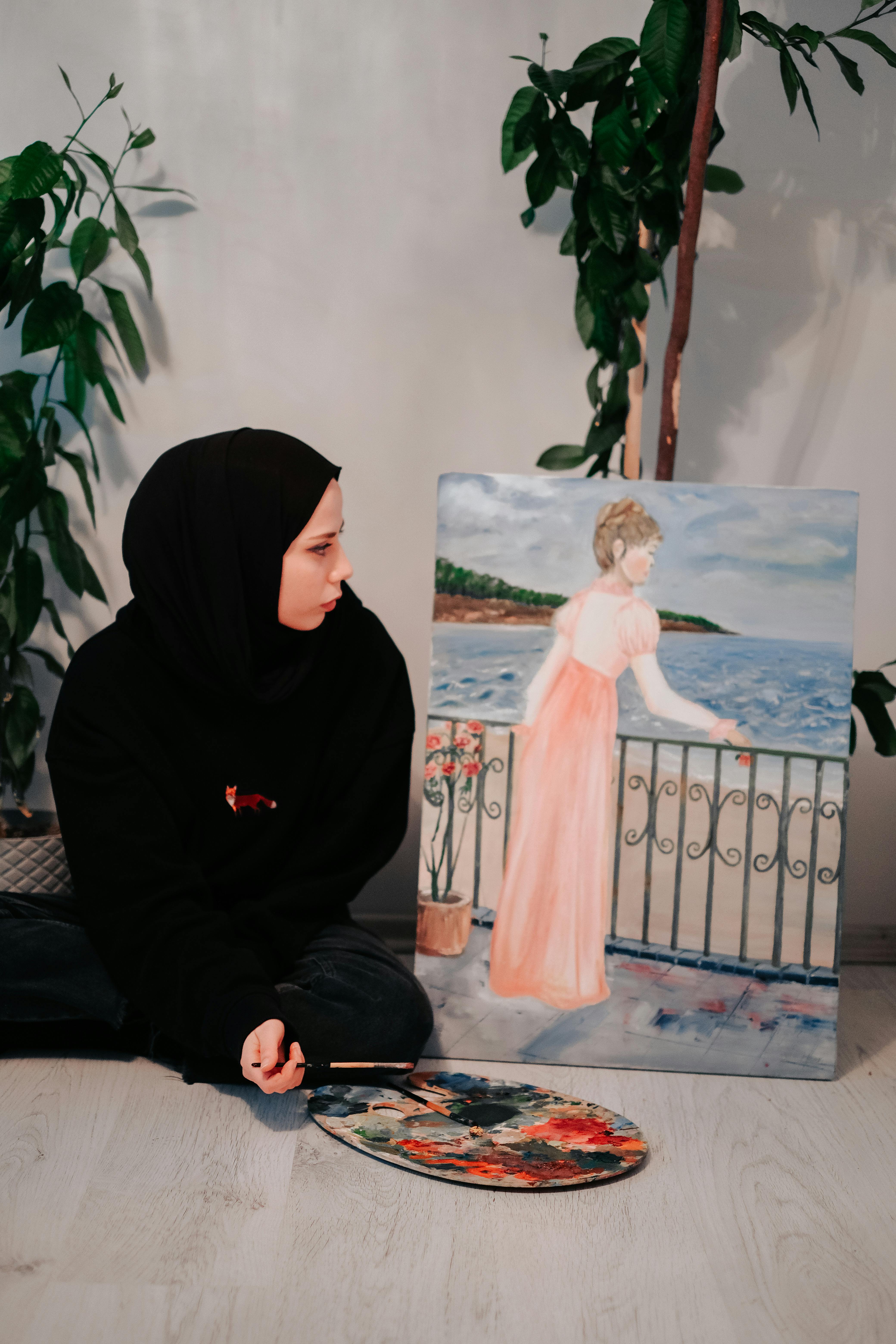 Young artist in studio with a watercolor painting of a woman by the sea, showcasing creativity.