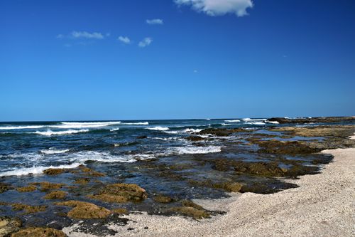 Free Beautiful rocky shoreline of Tamarindo Beach, Costa Rica with waves crashing under a clear blue sky. Stock Photo