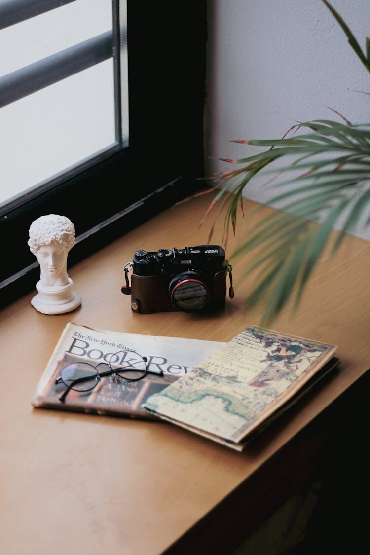 A Camera, A Map, A Book Review Newspaper And Eyeglasses Lying On A Windowsill