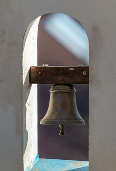 Close-up of a vintage brass bell in a stone archway, casting shadows.