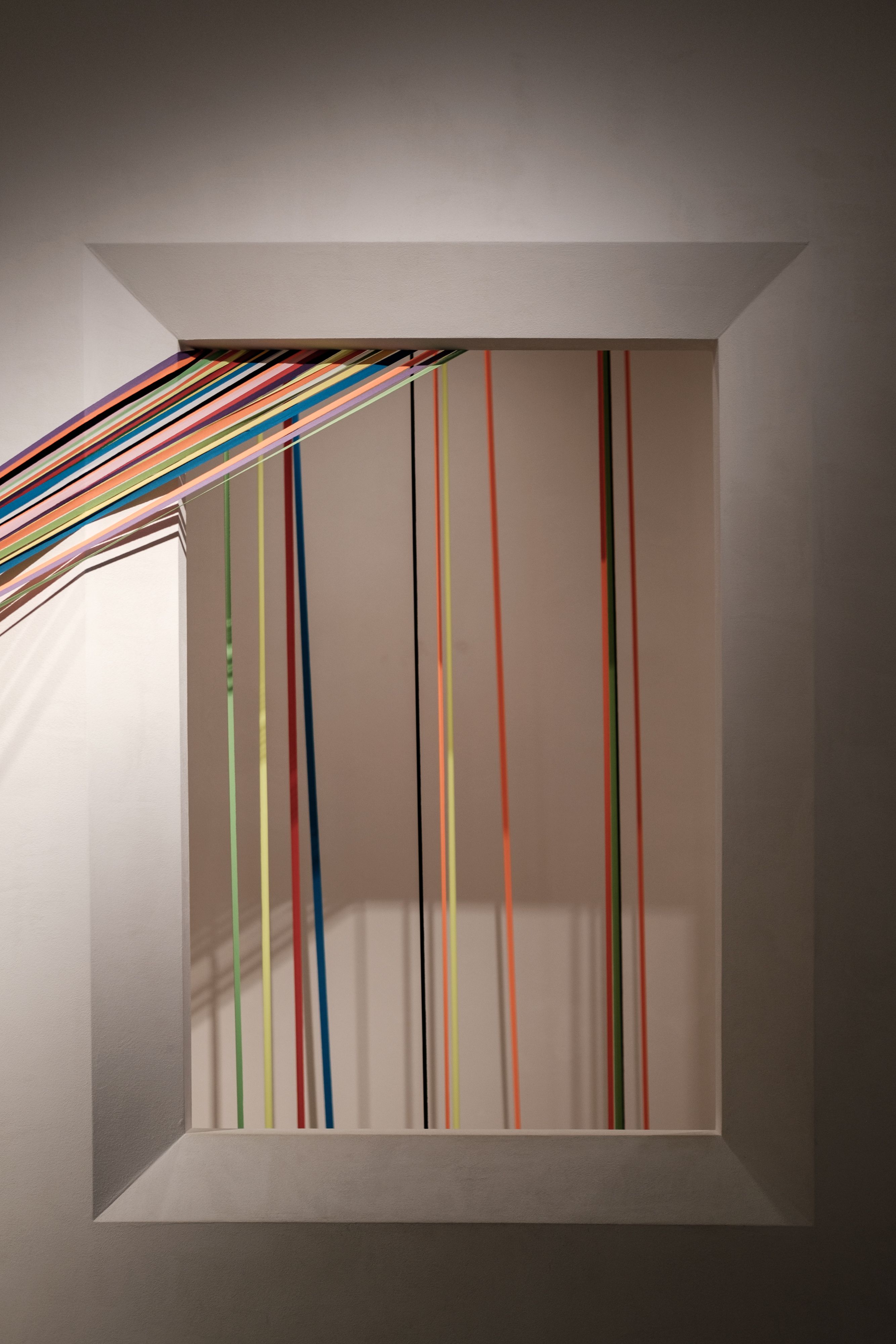 Vibrant art piece featuring colorful threads and a geometric frame against a gray wall.