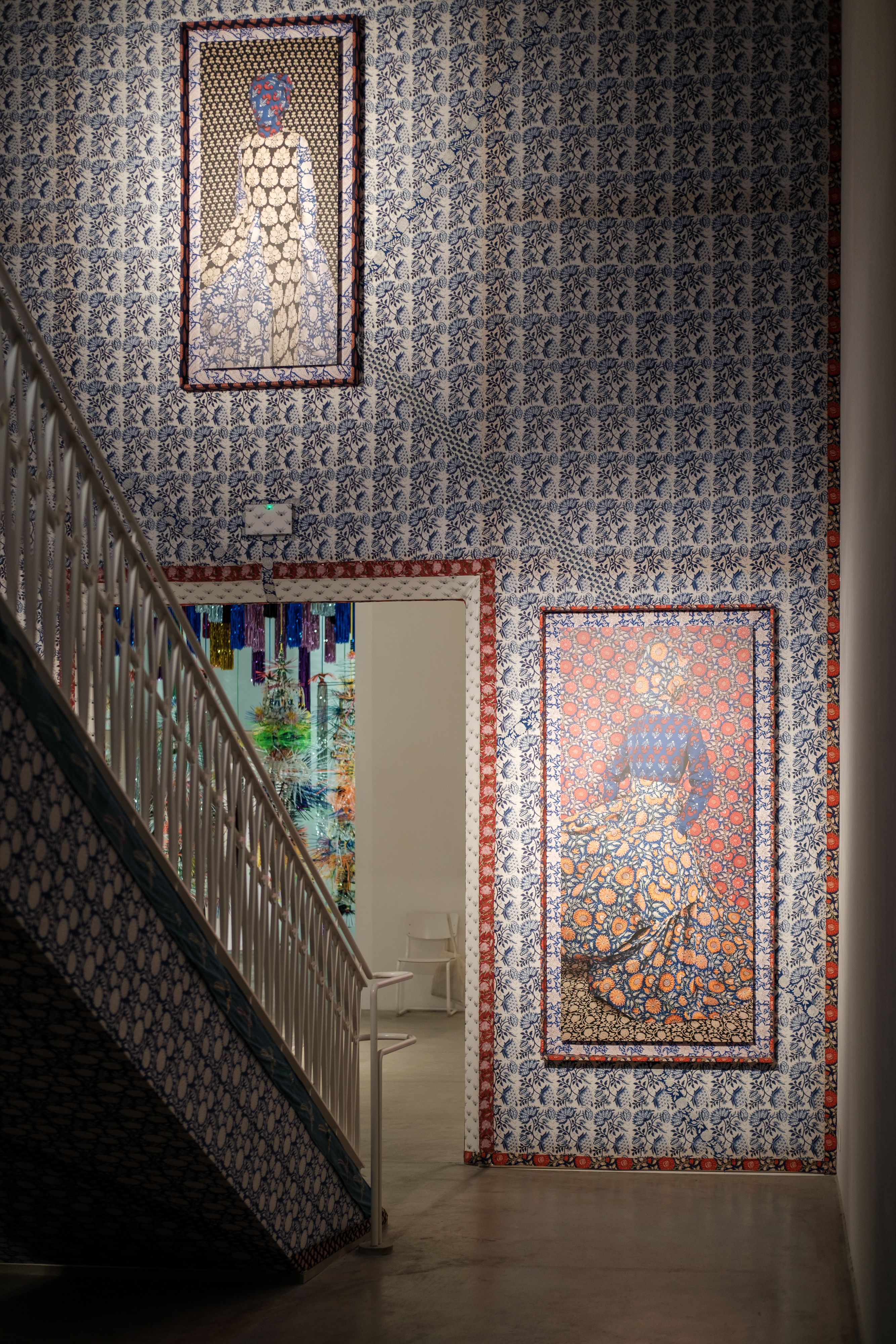 Artistic gallery with framed tapestries and intricate wallpaper on stairway walls.