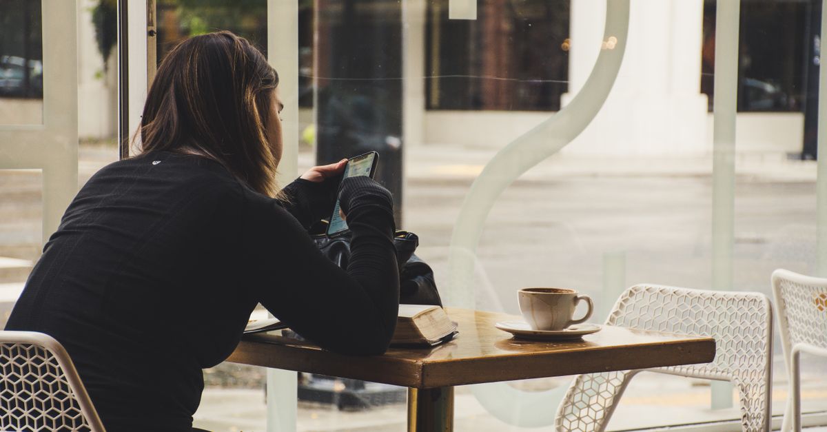 Person sitting by a window watching rain with a cup of coffee