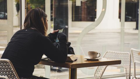 A woman enjoys coffee while using her smartphone at a cozy cafe table.
