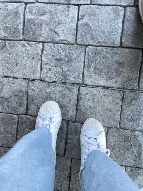 White sneakers and blue jeans on gray cobblestones in an outdoor setting.