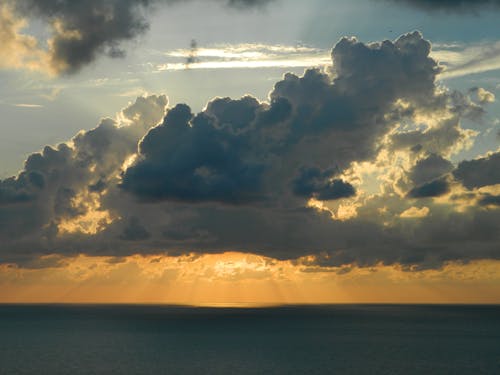 昼間の水域の上の白い雲の後ろの太陽